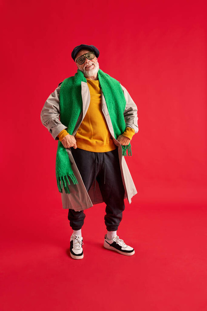 Full length photo of positive, adorable senior man with a beard in a bright outfit and glasses with hands on hips dancing with happiness. Concept of emotions, fashion, style, happiness, joy, mood - Fotó, kép
