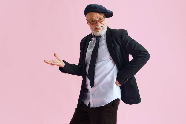 Portrait of senior bearded man dressed in casual style black jacket, nice sunglass and cap isoalated on pink color background. Concept of business, emotions, fashion, style. Ad. - Photo, Image