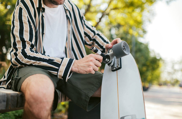 Stilvoller erwachsener Mann repariert sein Skateboard im Skatepark. Skateboard-Schlüssel - Foto, Bild