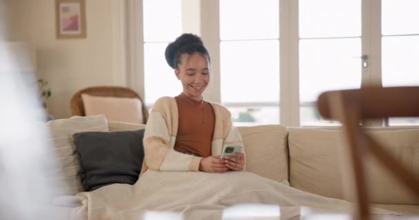 Young woman, phone and relax on sofa, thinking and blanket in home living room for texting, web chat or blog. Girl, excited smile and smartphone with scroll, meme or social media app on lounge couch. - Felvétel, videó