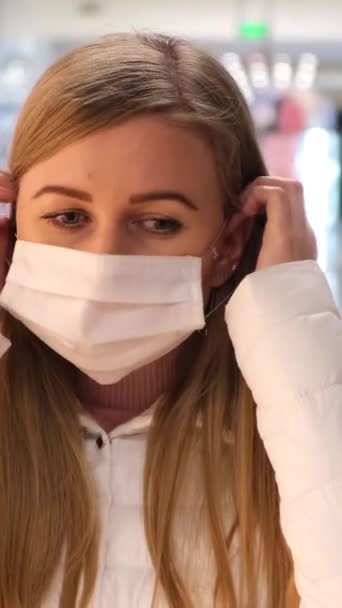Blondine vrouw zet een medisch masker op in een supermarkt en kijkt naar de camera, beschermt tegen het coronavirus. Gevaar voor coronavirusziekte COVID-19 - Video