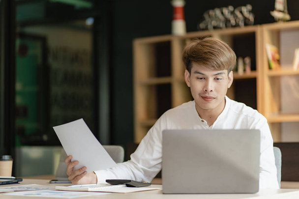 Azji młody człowiek wykonujący pracę księgową za pomocą aplikacji i dokumentów finansowych obliczających wynagrodzenie pracowników firmy i spotkania online. - Zdjęcie, obraz