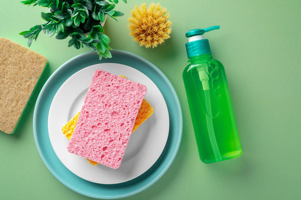 Cleaning sponge on plate with dishwashing liquid soap and  natural brush on green background, top view - Photo, Image