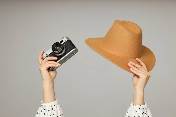 Vintage camera en hoed in vrouwelijke handen op grijze achtergrond - Foto, afbeelding