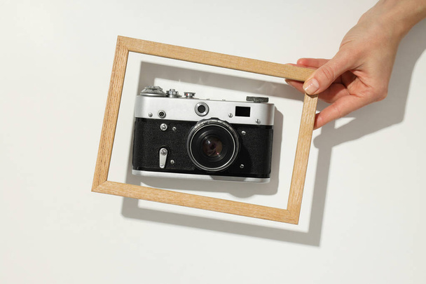 Vintage camera en fotolijstje in vrouwelijke hand op witte achtergrond, bovenaanzicht - Foto, afbeelding