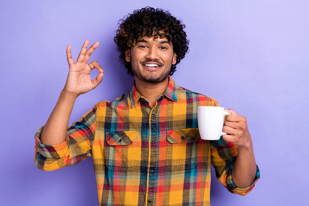 Portrait of handsome guy hold fresh aroma coffee mug demonstrate okey symbol isolated on purple color background. - Photo, image