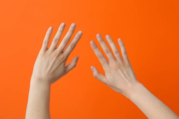 Δύο θηλυκά χέρια με απλωμένα δάχτυλα σε πορτοκαλί φόντο - Φωτογραφία, εικόνα