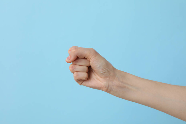 Mão feminina cerrada em um punho em um fundo azul claro - Foto, Imagem
