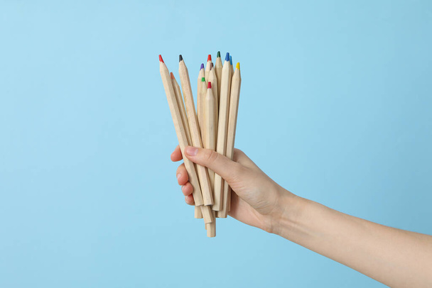 Жіноча рука тримає різнокольорові олівці на синьому фоні - Фото, зображення