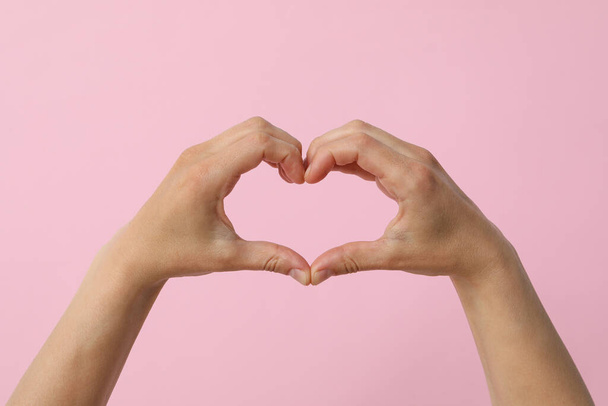 Les mains féminines font un signe cardiaque avec les doigts sur un fond rose - Photo, image