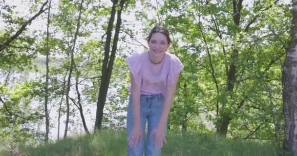 Experience the exuberance of a young womans playful moment in the woods with this heartwarming footage. The camera zooms in on her as she bends forward, hands on knees, her radiant smile capturing - Footage, Video