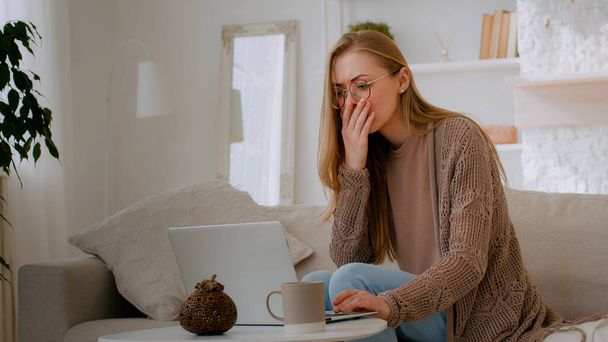 Кавказская шокированная женщина в очках, глядя на ноутбук и читая плохие новости, закрывает рот руками, держа голову, а студентка, потерявшаяся с компьютером, беспокоится о бизнес-проблеме - Фото, изображение