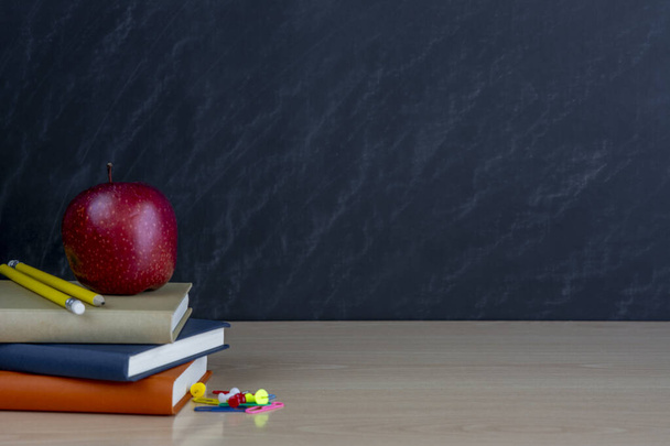Una pila de libros, una manzana roja y colorido, útiles escolares, sobre un fondo negro de la pizarra con un lugar para la inscripción. - Foto, imagen