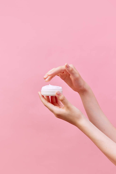 Cropped view of female hands holding container with cream in hands. Using cosmetics product isolated pastel pink background. Concept of body and skin care, spa, dermatology. Copy space for ad - Photo, Image