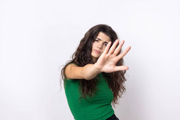 Retrato de una joven seria mostrando un gesto de stop con su palma sobre fondo blanco - Foto, imagen