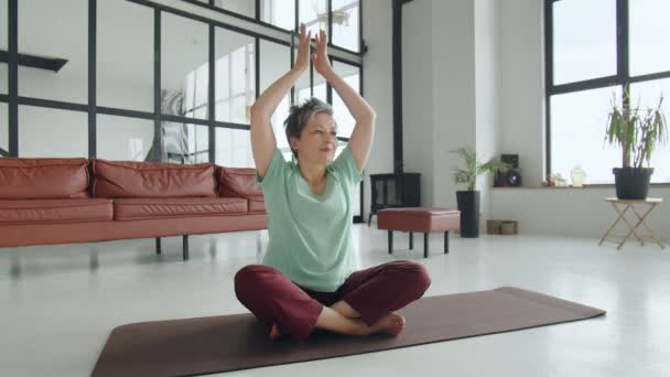 Стара жінка робить вправи на йогу вдома. Зріла жінка має медитацію в студії. Розслабте її тіло і розум, щоб звільнити все погане в її житті. Високоякісні 4k кадри - Кадри, відео