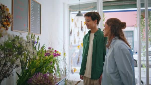 Joyful lovers shop flowers in florist store. Multiracial couple buy bouquet in floral shop closeup. Young flower buyers enjoy talk in light spring plant boutique. Chill romantic nature beauty concept. - Footage, Video
