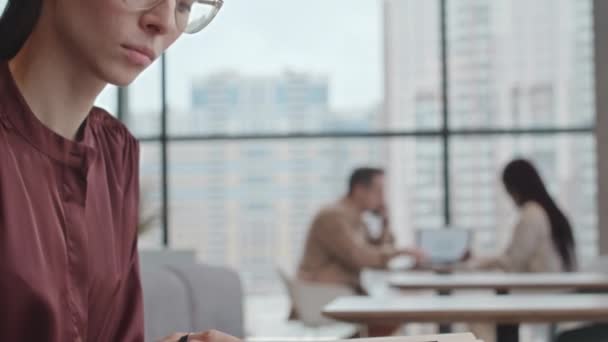 Plan incliné vers le bas de la jeune femme d'affaires réussie faisant de la paperasse à table dans un café avec des fenêtres panoramiques - Séquence, vidéo