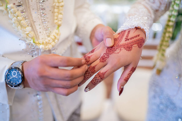 Un marito e una moglie si mettono le fedi nuziali a vicenda in una tradizionale cerimonia nuziale indonesiana. Lo sposo mette un anello al dito della sua amata moglie. La coppia si è scambiata le fedi. Appena sposata. - Foto, immagini