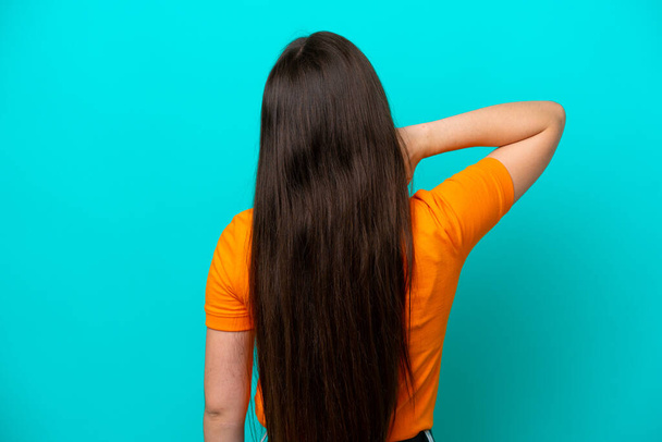 Giovane donna caucasica isolata su sfondo blu in posizione posteriore e pensando - Foto, immagini