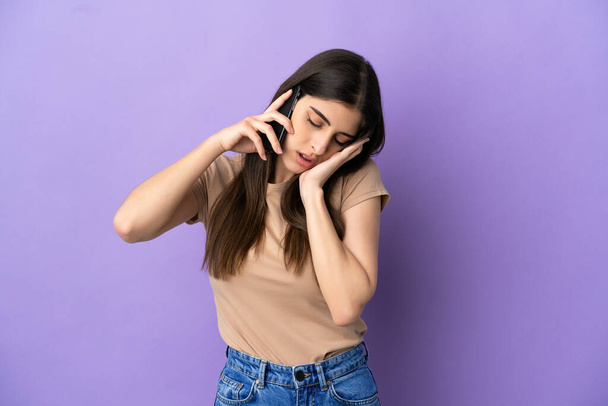 Молода біла жінка використовує мобільний телефон ізольовано на фіолетовому фоні з головним болем - Фото, зображення