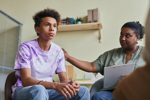 Afrikaanse tiener jongen praten tijdens groepstherapie sessie met psycholoog ondersteunen hem - Foto, afbeelding