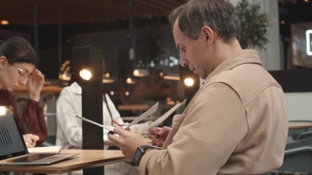 Diverse mensen zitten aan hun tafels in een modern café en werken op afstand - Video