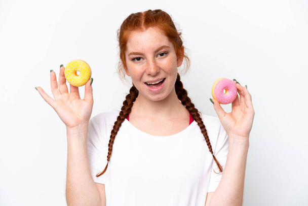 Young reddish woman isolated on white background holding donuts with happy expression - Foto, immagini