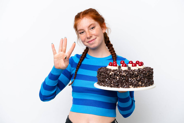 ホワイトバックグラウンドで孤立した誕生日ケーキを保持する若い赤みがかった女性は幸せで,指で4つを数えます - 写真・画像