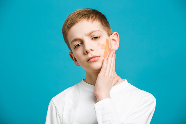 Unhappy boy in white clothes holding adhesive plaster on his che - Foto, Imagen