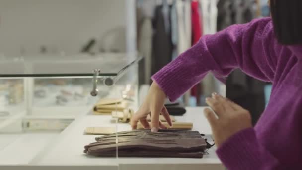 Foto recortada de asistente de tienda femenina que muestra artículos de accesorios de lujo bajo mostrador de vidrio mientras trabaja en la boutique de diseño - Metraje, vídeo