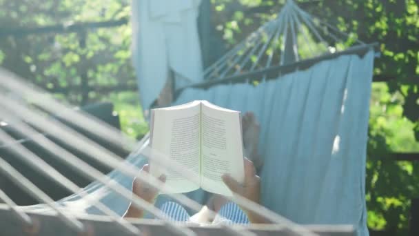 Красивая старшая блондинка читает книгу и отдыхает в гамаке в саду. Высококачественные 4k кадры - Кадры, видео