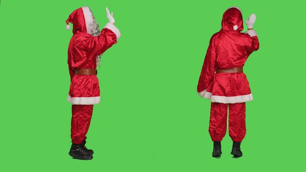 Happy Santa Claus aalto hei studiossa, yllään juhlava puku lasit ja punainen hattu yli koko kehon vihreys. Pyhä Nick tervehdys joku ja levittää loma henki. - Valokuva, kuva
