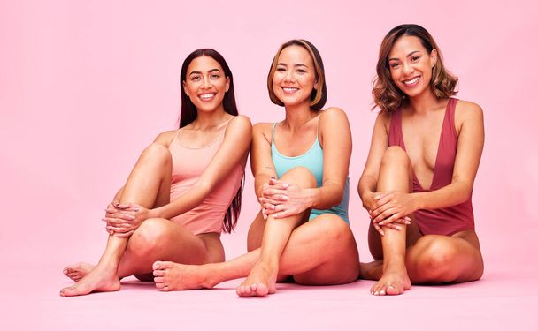 Beauty, bikini and group of women in studio, sitting together with smile and body positivity portrait. Diversity, summer fashion and happy swimwear models with self love, equality and pink background. - Photo, Image