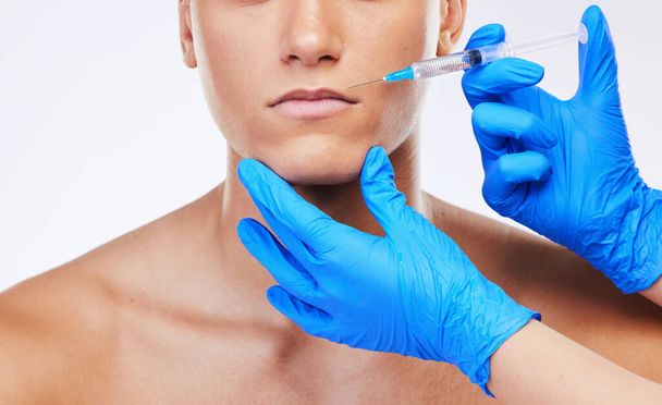 Man, syringe and lip filler surgery in studio with doctor for beauty, wellness or facial change by white background. Young model, needle and hands for mouth, cosmetic transformation and dermatology. - Photo, Image