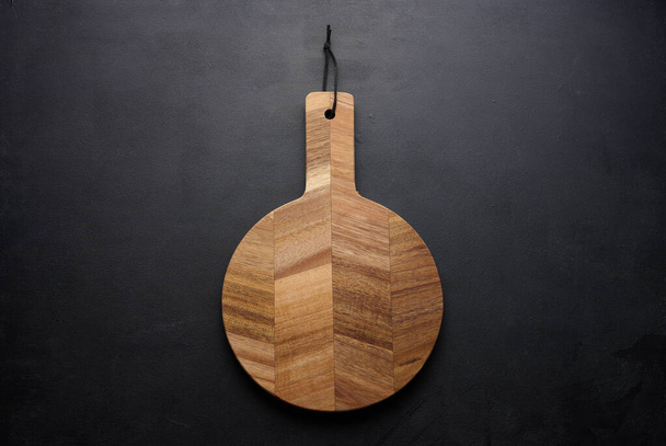 Planche à découper ronde de cuisine en bois avec poignée sur fond noir, vue de dessus - Photo, image