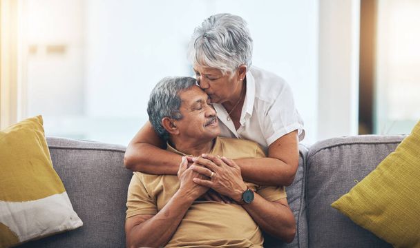 Aşk, öpücük ve kanepede oturan yaşlı çift sağlıklı bir evlilik ve oturma odasında ilişki için. Emeklilik, sarılma ve sevecen kadın ve erkek kanepede güven, bağlılık ve evde bakım için kucaklaşma. - Fotoğraf, Görsel