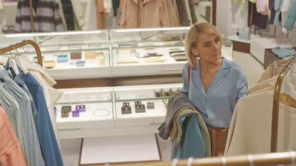 Plan poignardé d'une jolie femme blonde faisant des emplettes de vêtements et d'accessoires dans une boutique de créateurs de luxe - Séquence, vidéo