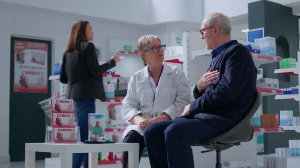 Elderly pharmacist in drugstore with senior patient after finishing annual examination, suggesting him medical products to treat illness symptoms. Older man receiving treatment from specialist - Footage, Video