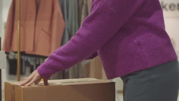Foto recortada de mujer irreconocible asistente de tienda desempacando mercancías en caja de cartón trabajando en boutique de diseño - Metraje, vídeo