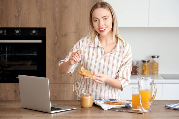 Jonge vrouw verspreidt lekkere notenboter op toast in de keuken - Foto, afbeelding