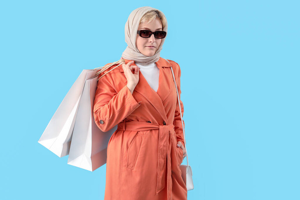 Stylish beautiful young woman with shopping bags on blue background - Zdjęcie, obraz