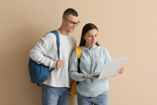 Gelukkige studenten met rugzakken met laptop op beige achtergrond - Foto, afbeelding