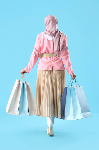 Mujer musulmana con bolsas de compras caminando sobre fondo azul, vista trasera - Foto, Imagen
