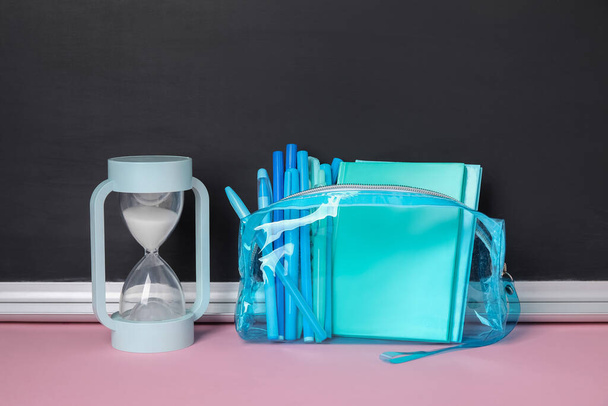 Pouzdro na tužky s různými školními kancelářemi a přesýpacími hodinami na růžovém stole u tabule - Fotografie, Obrázek
