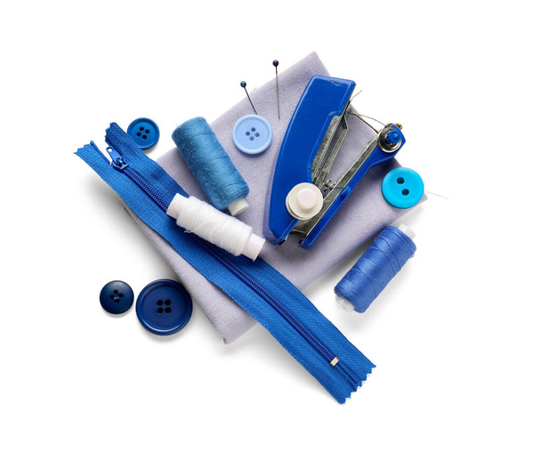 Ручная швейная машина с нитками, молнией, пуговицами и тканью на белом фоне - Фото, изображение