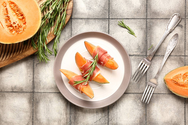 Plate of delicious melon with prosciutto and rosemary on grey tile background - Photo, Image