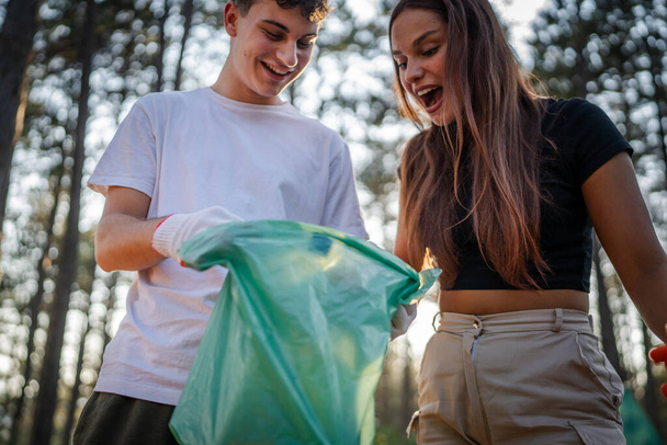 pár vagy tizenéves barátok gen Z férfi és női kaukázusi férfi nő felvette hulladék műanyag palackok és papír erdei takarítás természet napsütéses nap környezetvédelmi gondozás ökológia koncepció - Fotó, kép