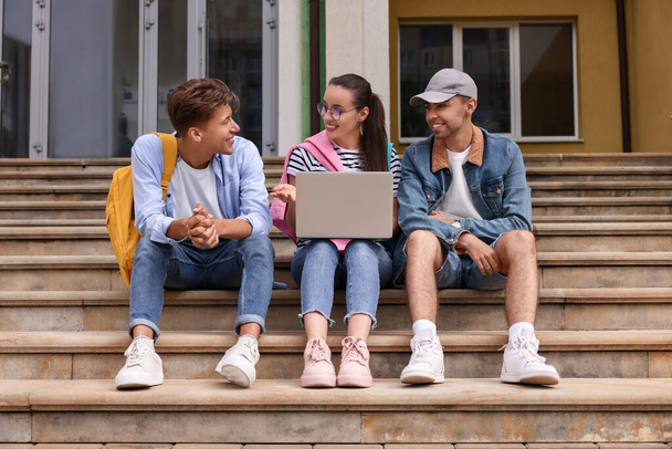 Happy young students studying together with laptop on steps outdoors - Foto, Bild