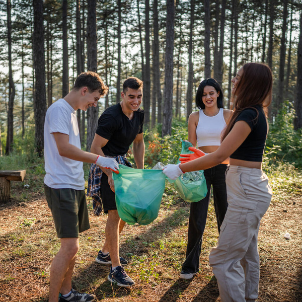 ティーンエイジャーの友人のグループ Z 男性と女性の慎重な男性 ゴミ捨てプラスチックボトルと森から紙を拾う女性 晴れた日の環境ケアのエコロジーの概念で自然をきれいにする - 写真・画像